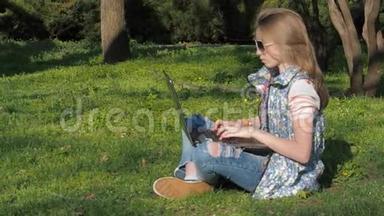 一个十几岁的女孩在草地上的公园里坐着一台电脑。 那个女孩坐在草地上的公园里。 在公园里阳光明媚的一天